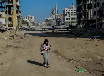 Salma, a 29-year-old, carries her infant while walking on Rashid Street, west of Gaza City, on 11 January 2024. 