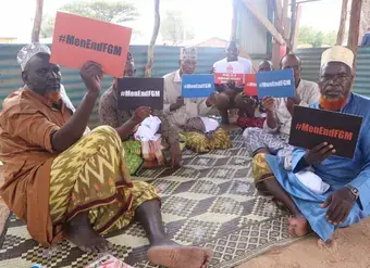 Men hold anti FGM signs at awareness training sessions