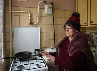 An elderly Ukrainian woman warms herself with a gas stove