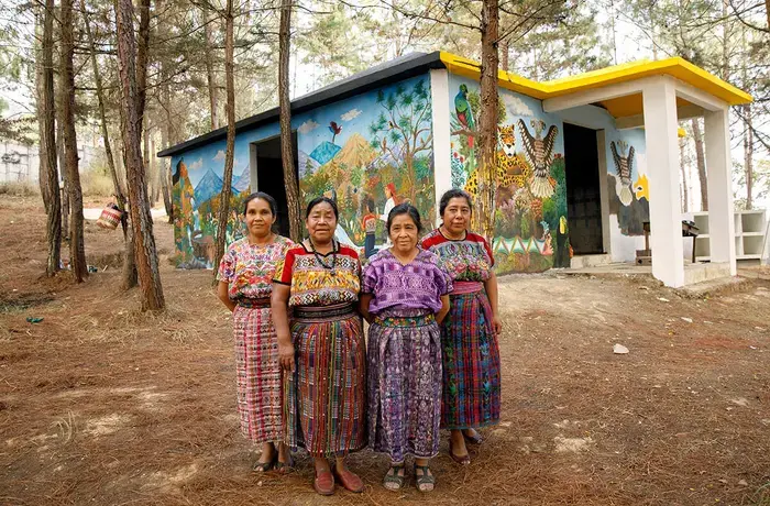 Artistas indígenas de San Juan Comalapa, Guatemala, pausan el trabajo de pintura y se toman una foto frente al Centro de la Memoria Histórica de las Mujeres, abril de 2018. En la foto, de izquierda a derecha: María Nicolasa Chex, Rosalina Tuyuc Velásquez, Paula Nicho Cumez, y María Elena Curruchiche. Foto: ONU Mujeres/Ryan Brown.