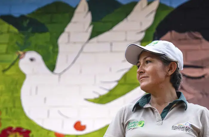 A woman stands in front of a painting of a dove. 