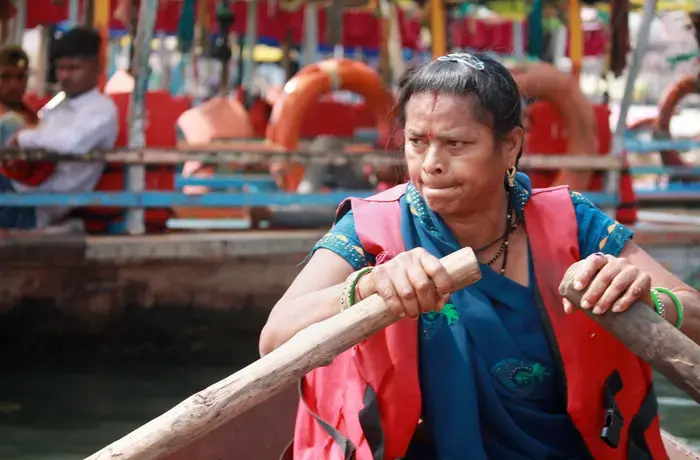 A woman, wearing an official tourist guide vest, steers a boat