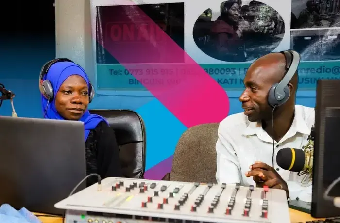 Two radio hosts, a woman and a man, talk in their recording room