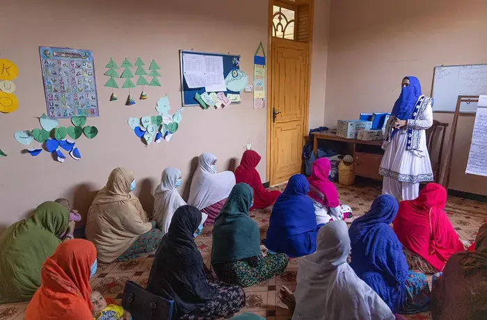 Afghan women sit on a classroom floor and listen closely to a teacher