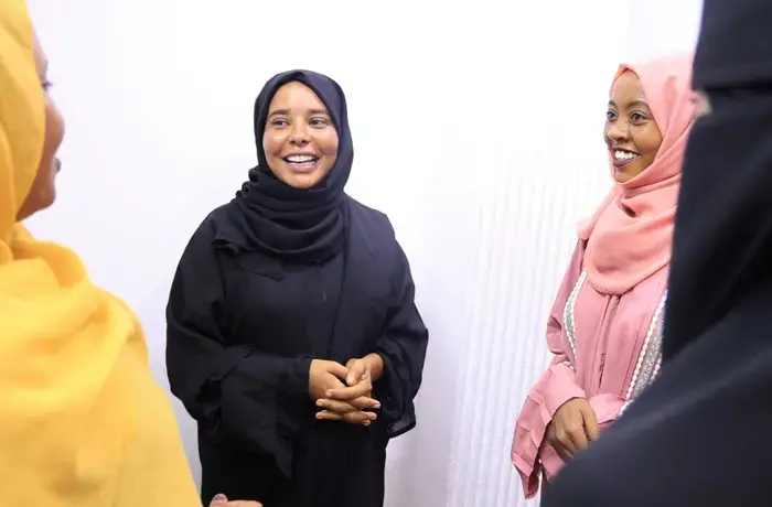 Four young women stand together, talking and laughing