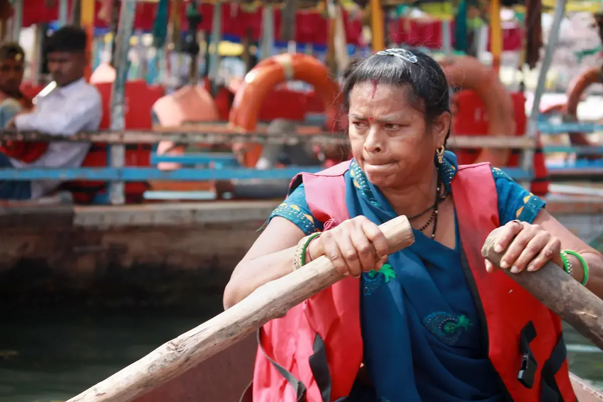 A woman, wearing an official tourist guide vest, steers a boat