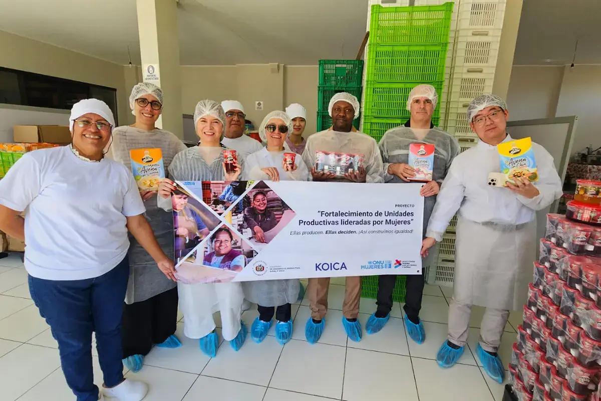 A group of people wearing protective clothing stand in a production facility holding packaged products and a project banner.