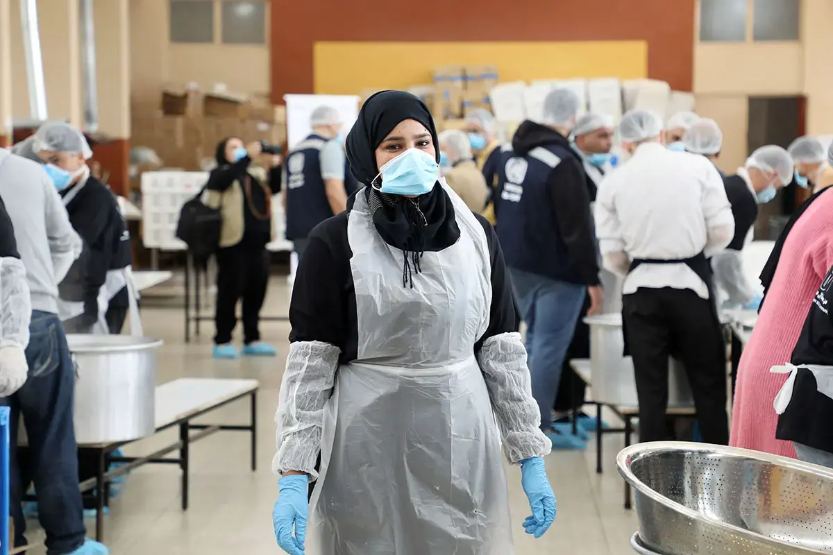 A woman wearing an apron and gloves stands in a community kitchen