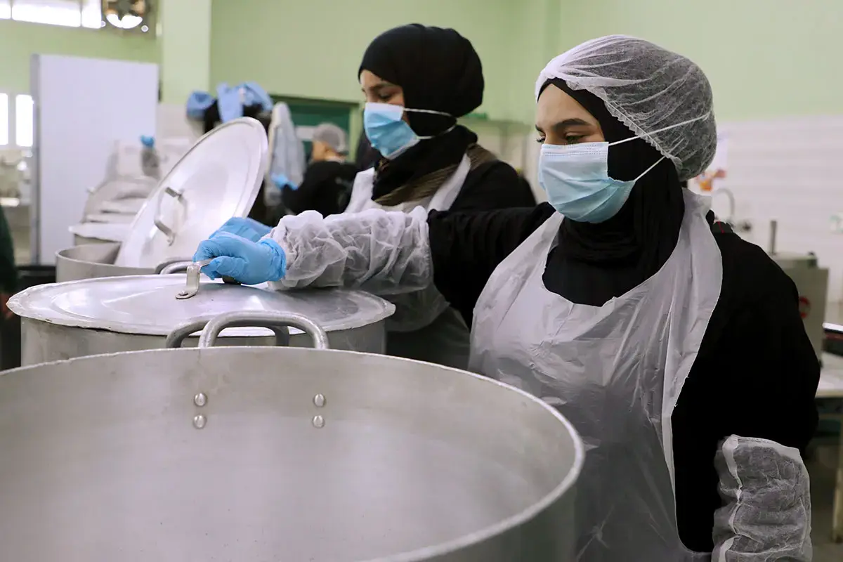 Two women stand over large cooking pots in a community kitchen