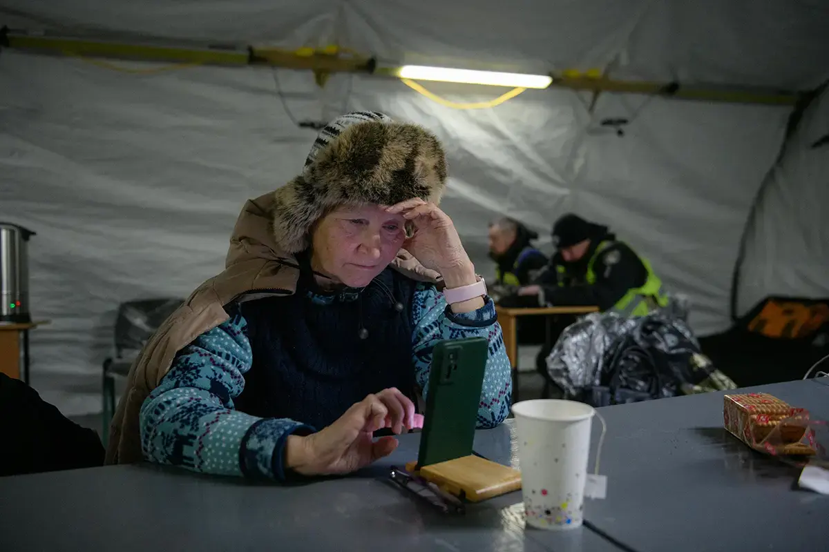 An older woman uses a mobile phone while seated inside a shelter.