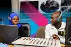 Two radio hosts, a woman and a man, talk in their recording room