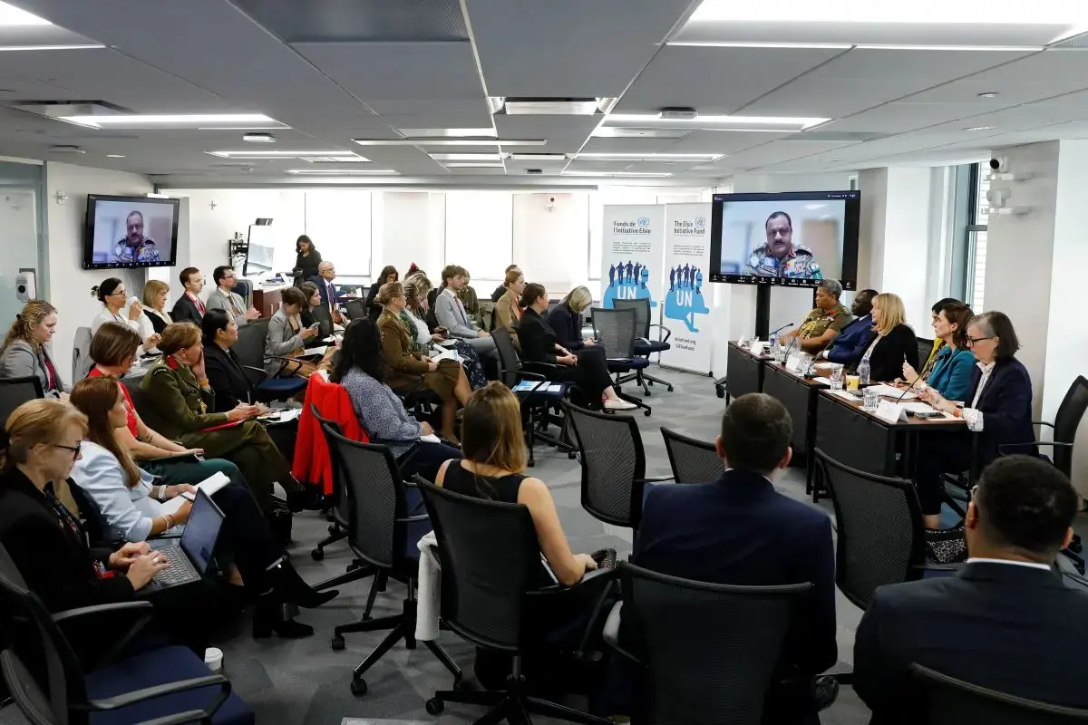 A man in military uniform speaks to an audience via teleconference