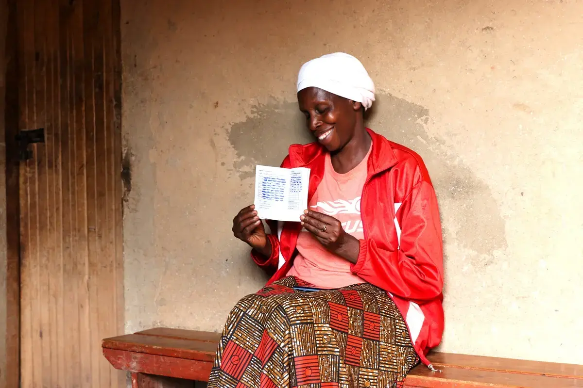Agnes proudly shows the VSLA record book, smiling as she points to the long list of loans, repayments, and savings registered in it.