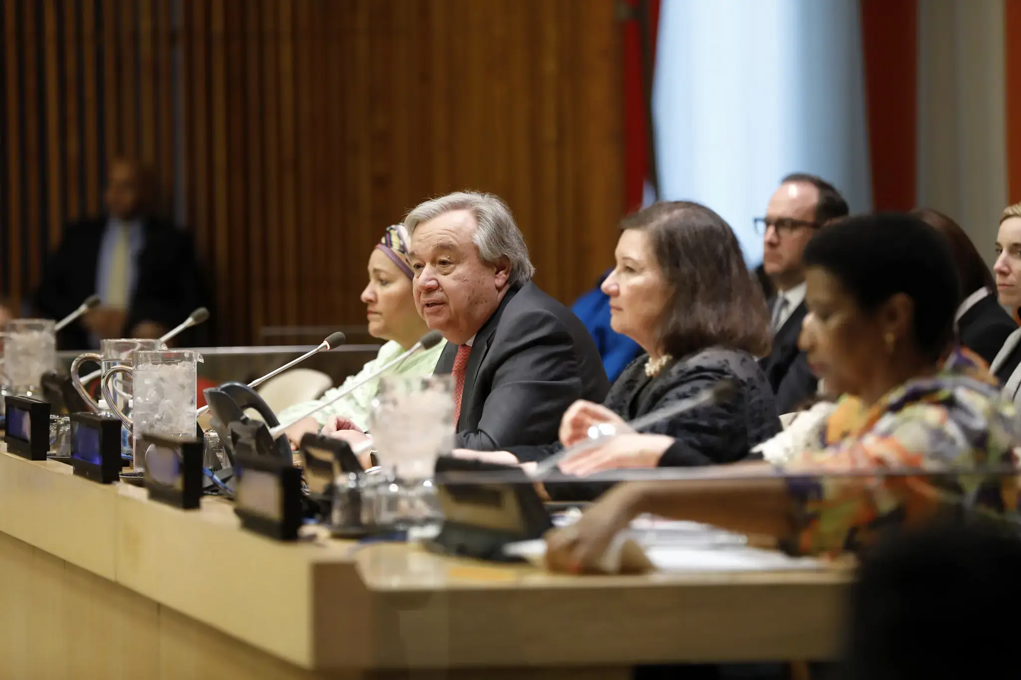 UN Secretary-General António Guterres speaking at a town hall meeting, seated at a conference table with a microphone in front of him.